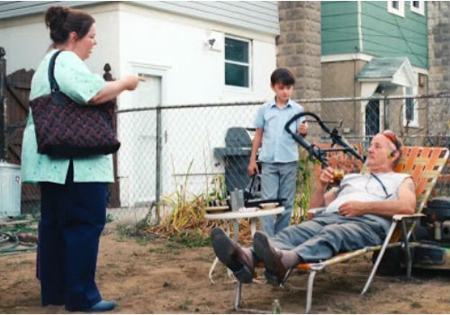 Maggie wanders across to Vincent's down-at-heel yard, a physical manifestation of the man himself, to find out why her son is mowing dirt while his caretaker sits there drinking alcohol (image via Teaser Trailer)